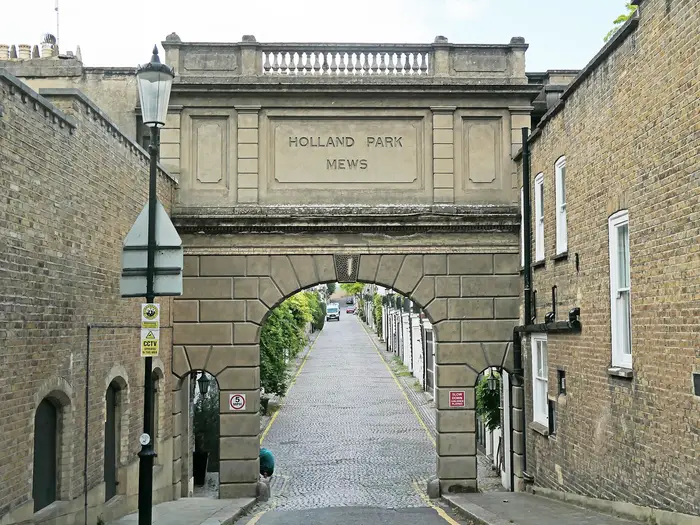 The stone entrance arch of Holland Park Mews over a cobbled mews