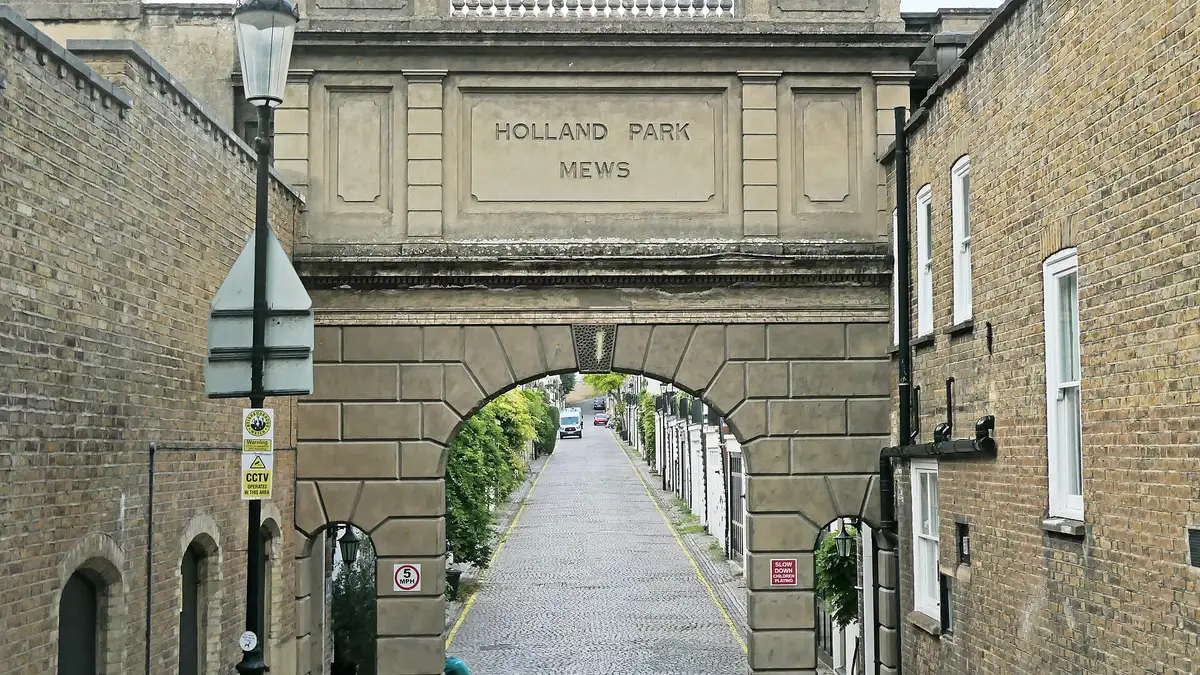 The stone entrance arch of Holland Park Mews over a cobbled mews